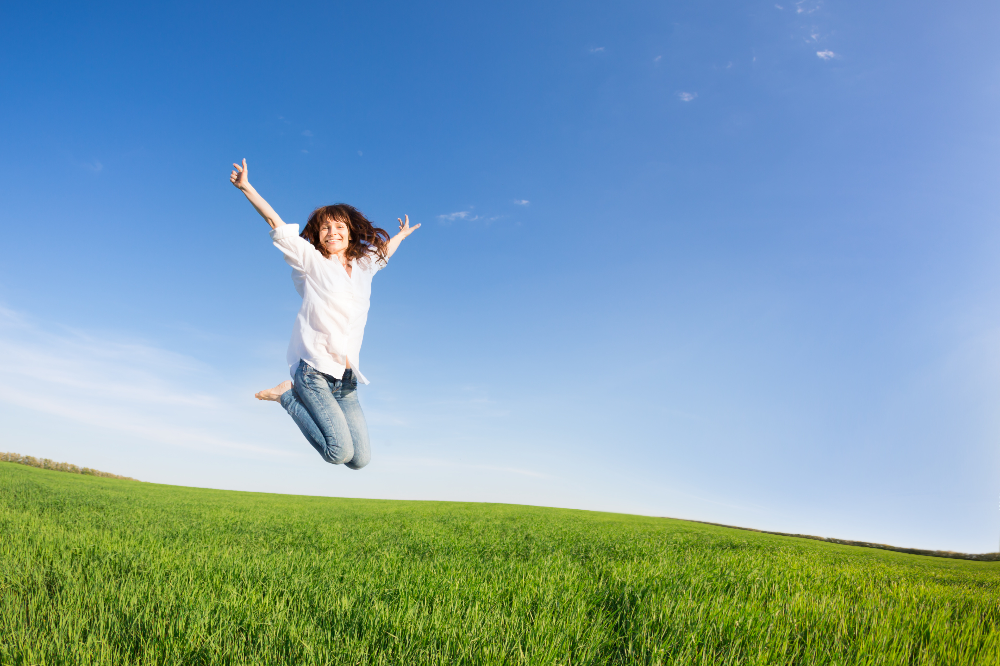 Happy woman jumping in green field against blue sky. Summer vacation concept
