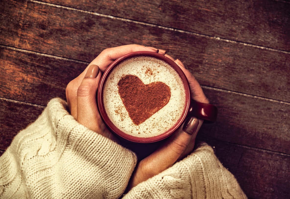 woman holding hot cup of coffee with heart shape symbol. Above view