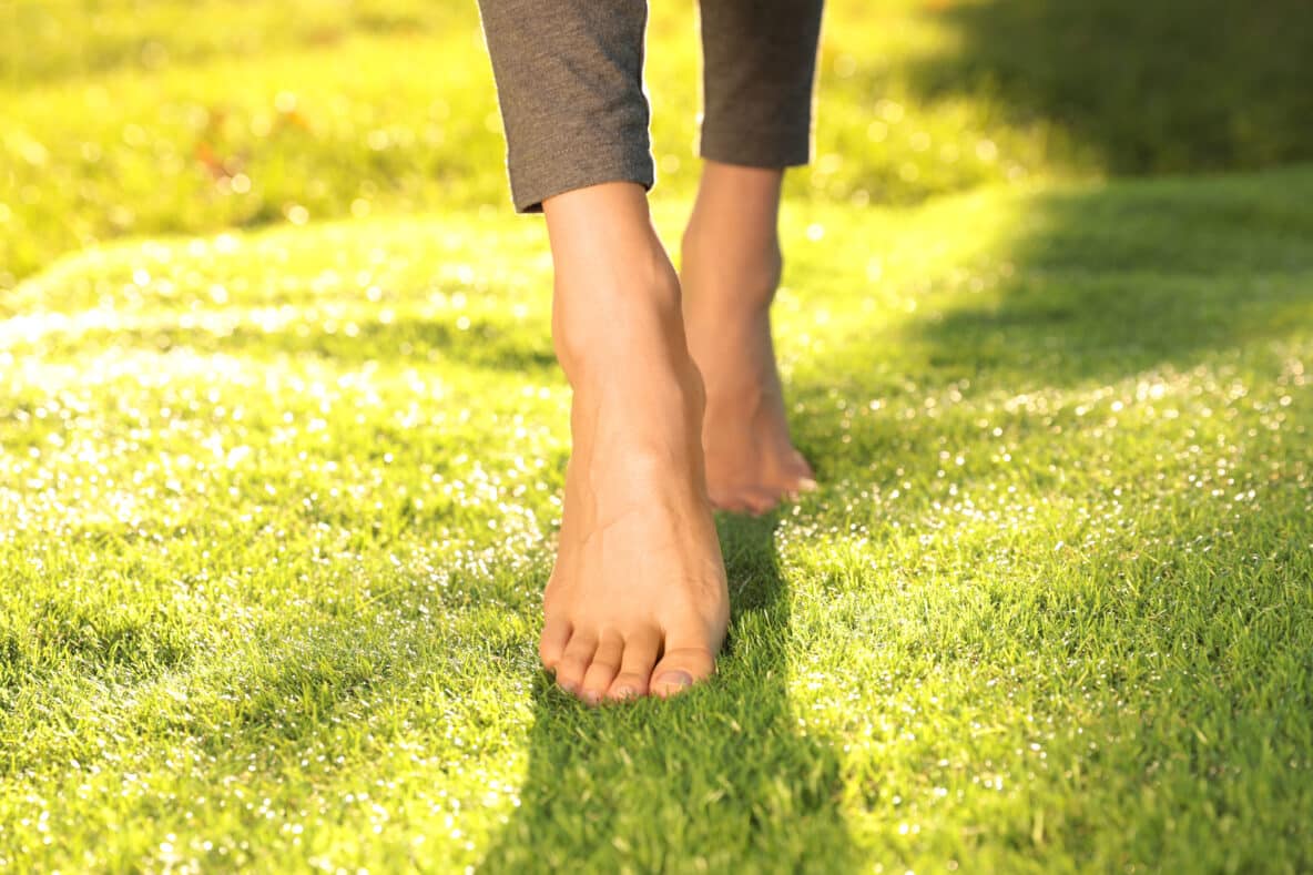 Young woman walking barefoot on fresh green grass, closeup